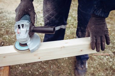 Tahta cilalamak için elektrikli öğütücü kullanan bir adam.