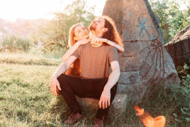 Hippi, romantik çift parkta eğleniyor. Öğleden sonra güneşinin tadını çıkarıyorum. Uzun saçlı kız arkadaşı olan kıvırcık saçlı erkek arkadaş..