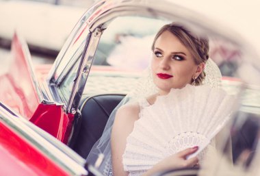 Beautiful bride inside a vintage red car looking thtough window