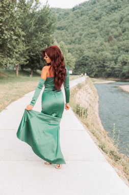 Zarif yeşil ipeksi elbiseli, balo için hazır genç bir kızıl kız. Arka plan