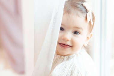 Perdenin arkasına bakan bir yaşındaki küçük bir kızın yakın plan portresi.