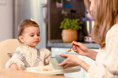 Genç anne bebeğini kaşıkla besliyor.