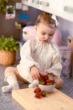 Küçük bebek mutfak masasında tek başına oturmuş çilek yiyor.