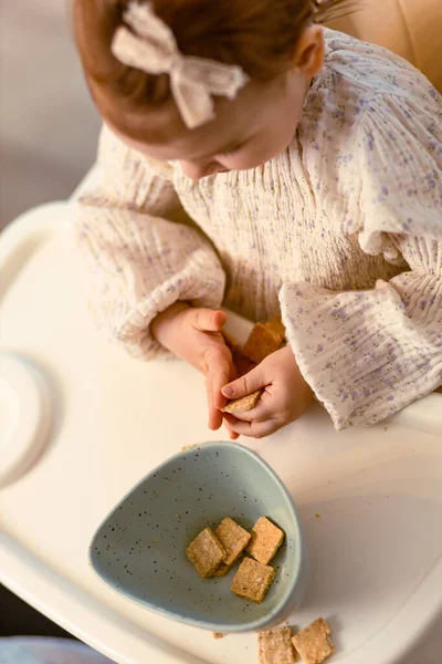 Kislány Aki Egy Etetőszékben Egyedül Kekszet Eszik Stock Kép