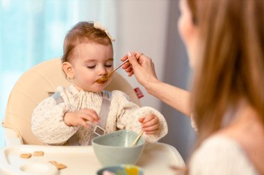 Genç anne bebeğini kaşıkla besliyor.