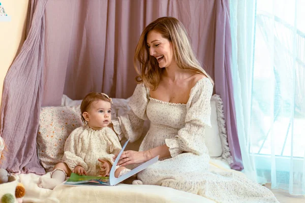 Genç anne bir yaşındaki kızıyla kitap okuyor.