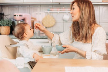 Genç anne bebeğini kaşıkla besliyor.