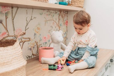 Küçük bir kız bebek masada oturmuş küçük oyuncaklarla oynuyor. Boşluğu kopyala