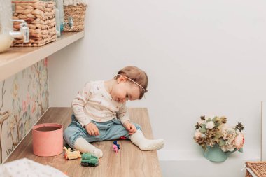 Küçük bir kız bebek masada oturmuş küçük oyuncaklarla oynuyor. Boşluğu kopyala