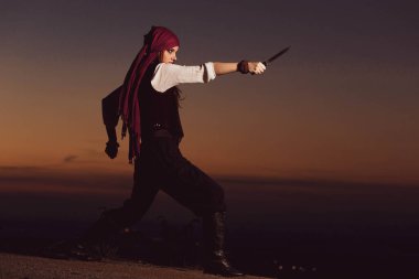 Outdoor portrait of young female in pirate costume holding a knife clipart