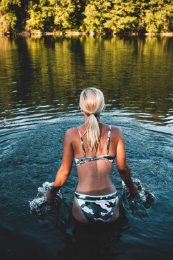 Sarışın kadın yüzmeye gitmeden önce nehir suyunda duruyor.