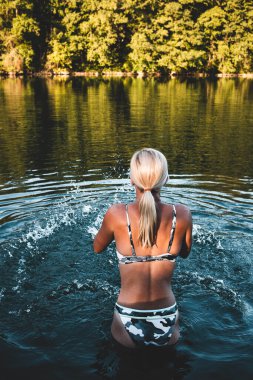 Sarışın kadın yüzmeye gitmeden önce nehir suyunda duruyor.