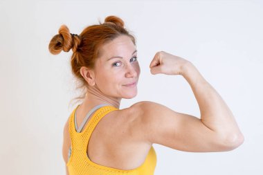 Genç, sarışın, fit bir kadın kaslarını gösteriyor.