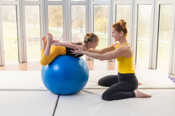 Young fit mom and her daughter having fun with fitness ball in a gym