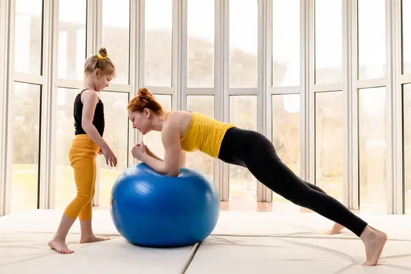 Young fit mom and her daughter having fun with fitness ball in a gym