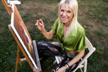 Açık havada resim yapan genç, sarışın kadın.