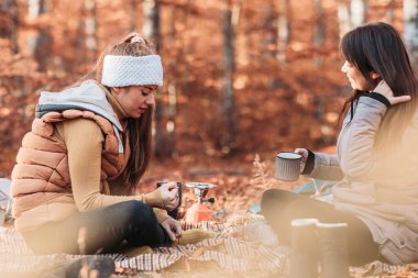 Two girls drinking hot tea from metal cups outdoor, camping