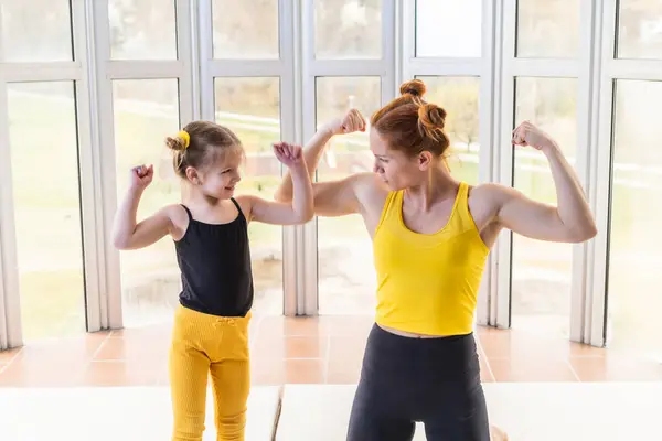 Young fit mom and her daughter in matching clothes, showing muscles. Fitness motivation