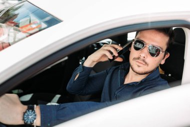 Genç adam arabasının içinde telefonla konuşuyor.
