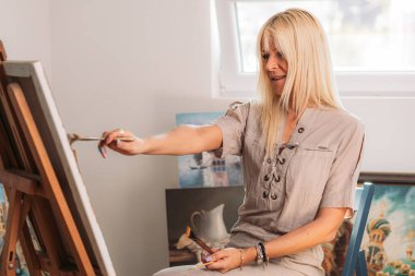 Atölyesinde resim yapan genç, sarışın bir kadın.