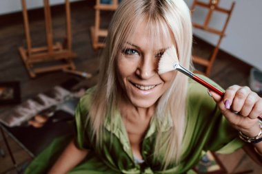 Genç sarışın kadın ressam, bir fırçayla gözlerini kapatıyor.