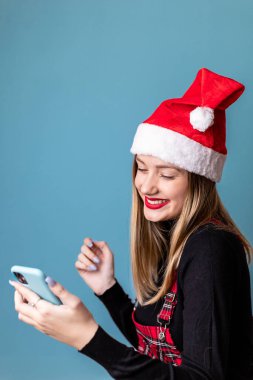 Noel Baba şapkalı genç, sarışın kız telefonuna bakıyor.