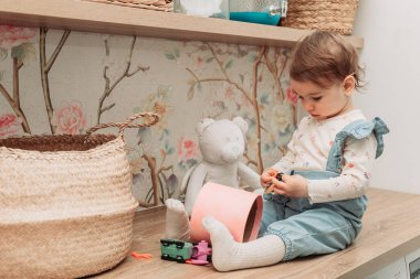 Küçük bir kız bebek masada oturmuş küçük oyuncaklarla oynuyor. Boşluğu kopyala