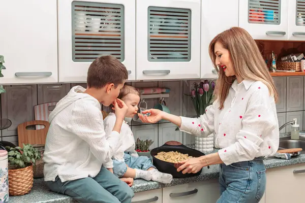 Mom and her children in the kitchen with pasta in the pan for dinner