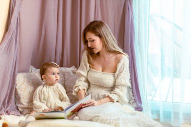 Genç anne bir yaşındaki kızıyla kitap okuyor.