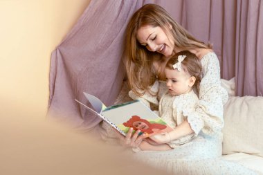 Genç anne bir yaşındaki kızıyla kitap okuyor.