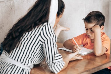 Little school boy doing homework with his mom helping him