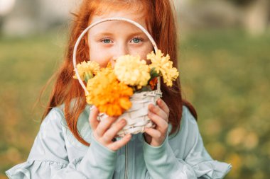 Kızıl, kızıl saçlı kız elinde turuncu ve sarı çiçekli bir sepet tutuyor.