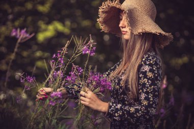 Sarı şapkalı genç kız mor çiçekleri topluyor.