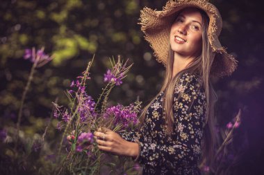 Sarı şapkalı genç kız mor çiçekleri topluyor.