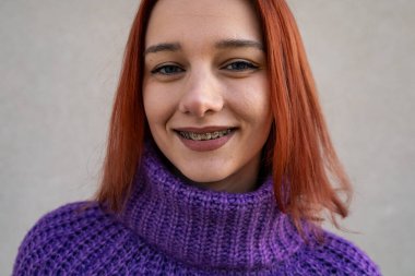 Gülümseyen, parlak kollu, mor süveterli genç bir kadın.