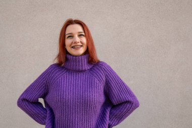 Mor örgülü balıkçı yaka kazak içinde gülümseyen neşeli kızıl saçlı kadın.