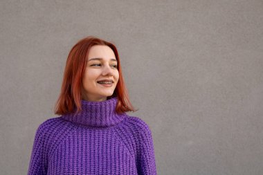 Mor örgülü balıkçı yaka kazak içinde gülümseyen neşeli kızıl saçlı kadın.