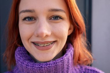 Mor örgülü balıkçı yaka kazak içinde gülümseyen neşeli kızıl saçlı kadın.