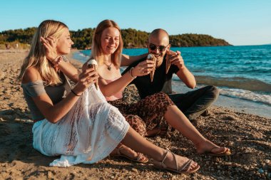 Güneşli bir sahilde dondurmanın tadını çıkaran üç arkadaş.