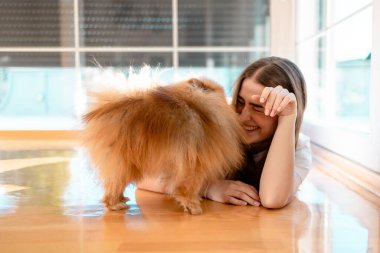 Gülümseyen genç kadın yerde yatıyor pomeranya köpeğiyle oynuyor.