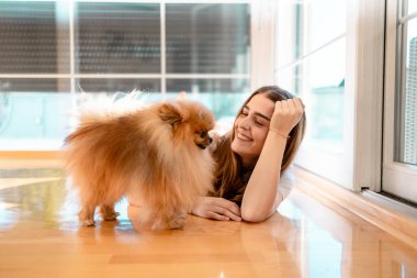 Gülümseyen genç kadın yerde yatıyor pomeranya köpeğiyle oynuyor.