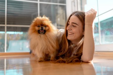 Gülümseyen genç kadın yerde yatıyor pomeranya köpeğiyle oynuyor.