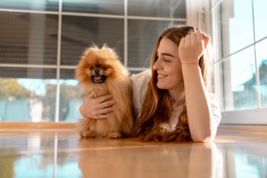 Gülümseyen genç kadın yerde yatıyor pomeranya köpeğiyle oynuyor.