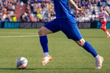 Futbolcu rekabetçi bir maçta topu sürüyor.