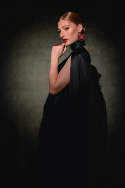 Kızıl saçlı, çilli, çenesine dokunan ve kasvetli bir moda stüdyosunda kameraya bakan bir kızın profili..