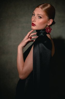 Kızıl saçlı, çilli, çenesine dokunan ve kasvetli bir moda stüdyosunda kameraya bakan bir kızın profili..