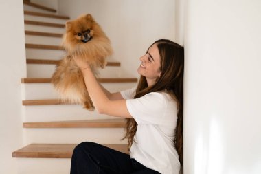 Pomeranya köpeğiyle merdivenlerin yanında oynayan bir kadın.