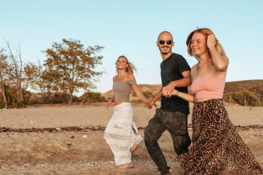 Gün batımında Potos, Thassos 'ta plajda koşan üç mutlu arkadaş.