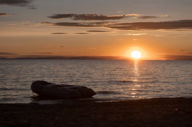 Deniz üzerinde sakin bir günbatımı manzarası ve kıyıda sürüklenen dallar.