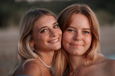 Sahilde altın saatinde gülümseyen iki genç kadının yakın plan portresi.
